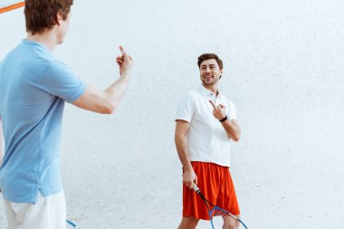 Birbirlerine orta parmakları gösteren squash oyuncuları kırpılmış görünümü
