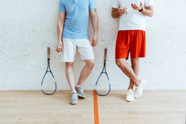 Dört duvarlı kortta çapraz bacaklarla ayakta şort iki squash oyuncu kırpılmış görünümü