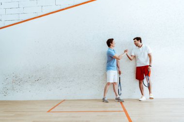 Dört duvarlı kortta el sıkışırken squash oyuncularının tam boy görünümü