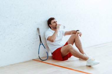 Yerde oturan ve su içme kırmızı şort Squash oyuncu