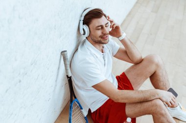 Gülümseyen squash oynatıcı yerde oturan ve kapalı gözlü kulaklık müzik dinleme