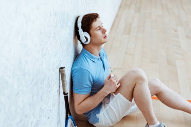 Squash oyuncu katta oturan ve kapalı gözlerle müzik dinleme