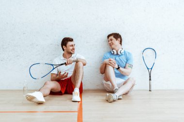 Dört duvarlı sahada yerde otururken iki squash oyuncusu konuşuyor