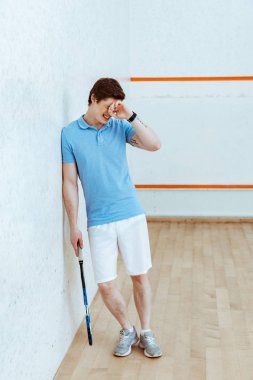 Dört duvarlı kortta el ile gözleri dokunmadan üzgün squash oyuncu tam uzunlukta görünümü