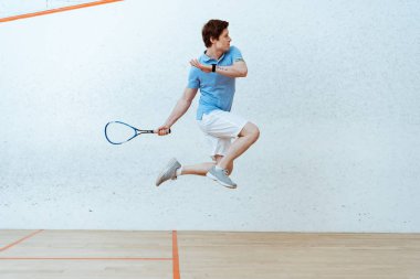 Sportsman in polo shirt jumping while playing squash in four-walled court clipart