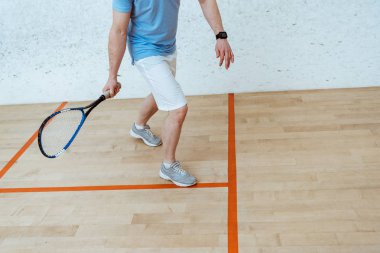 Dört duvarlı kortta squash oynayan raketile sporcu kısmi görünümü