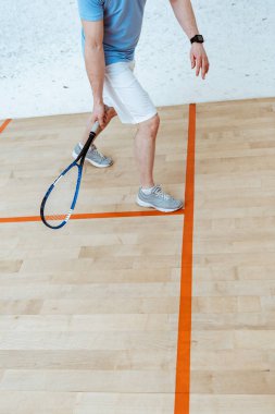 Partial view of sportsman with racket playing squash in four-walled court clipart