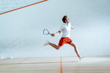 Full length view of sportsman with racket running while playing squash clipart