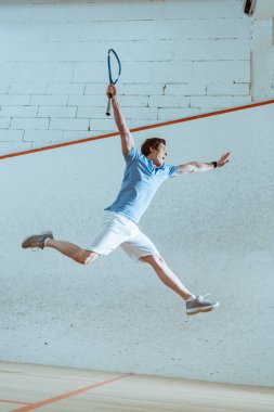 Full length view of excited sportsman in blue polo shirt jumping while playing squash clipart