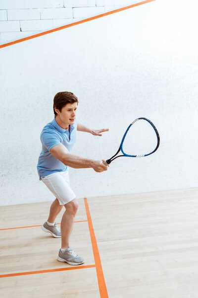 Emotional sportsman in blue polo shirt playing squash in four-walled court