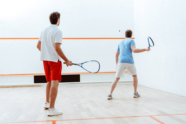 Back view of two sportsmen playing squash in four-walled court