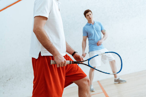 Cropped view of squash players with rackets in four-walled court