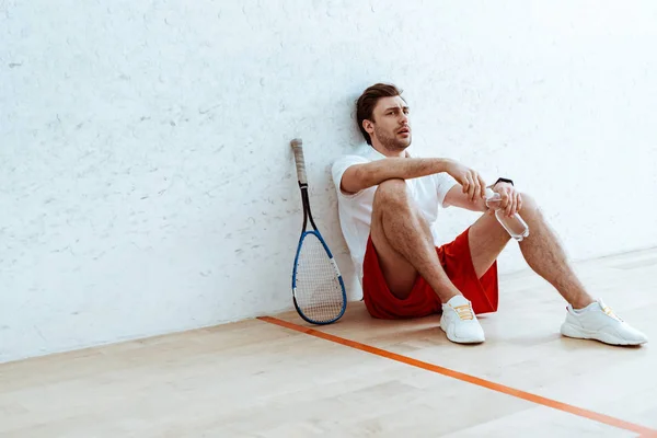 Squash Player Seduto Sul Pavimento Con Mano Una Bottiglia Acqua — Foto Stock