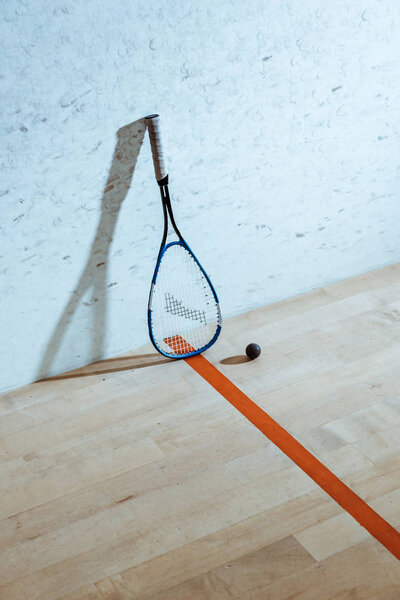 One squash racket and ball on wooden floor in four-walled court