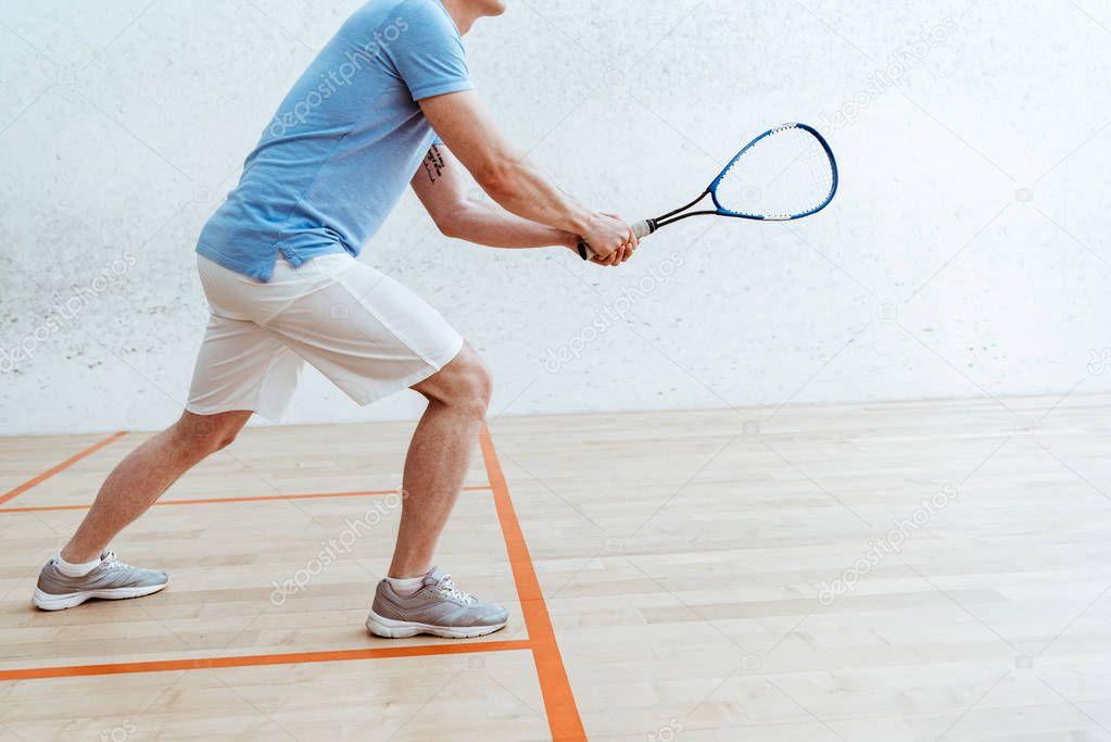 Cropped view of sportsman in blue polo shirt playing squash in sports center