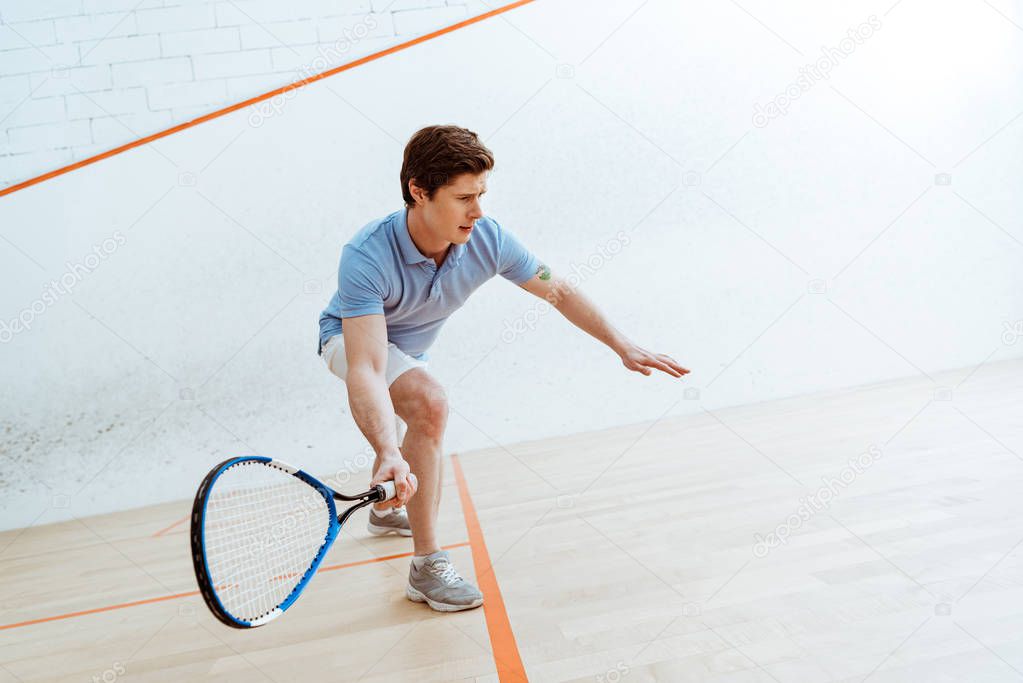 Emotional sportsman in blue polo shirt playing squash in four-walled court