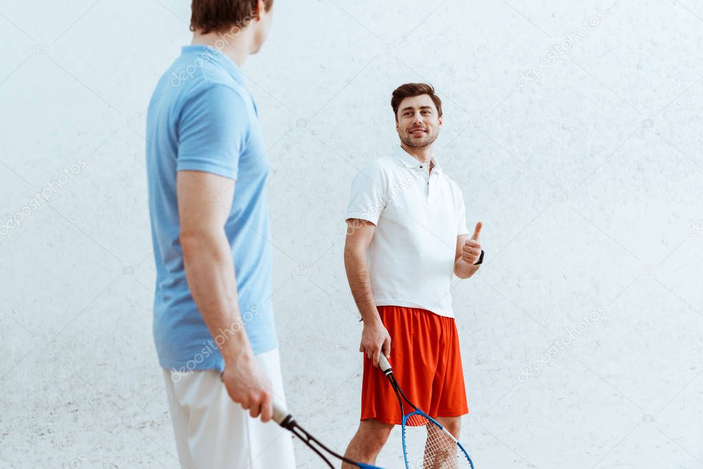 Smiling squash player in red shorts showing thumb up to opponent