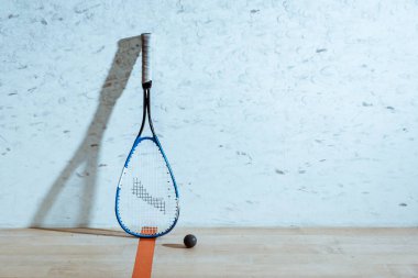 One squash racket and ball on wooden floor in four-walled court clipart
