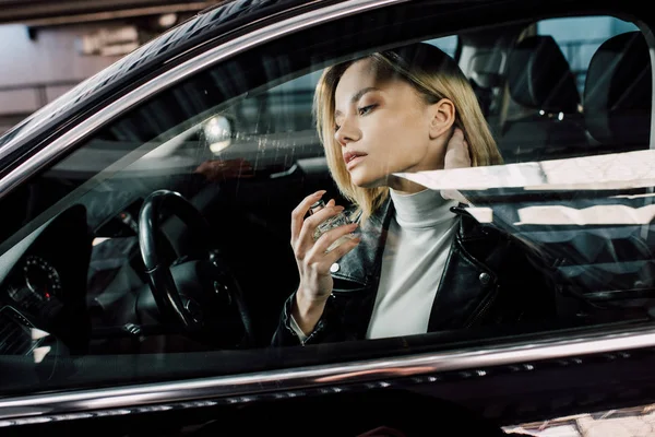 車の中で香水を吹き付けながらボトルを保持している魅力的なブロンドの女性 — ストック写真