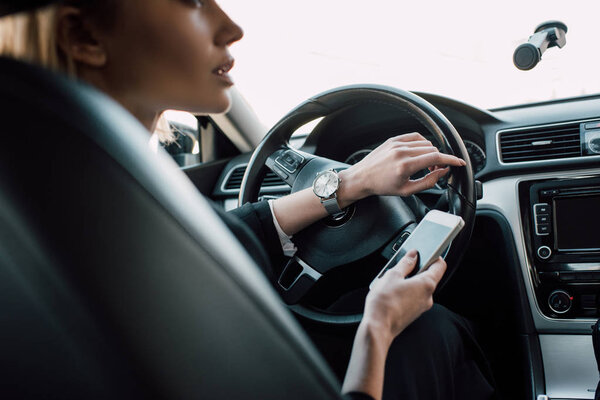 cropped view of blonde woman sitting in car and holding smartphone 