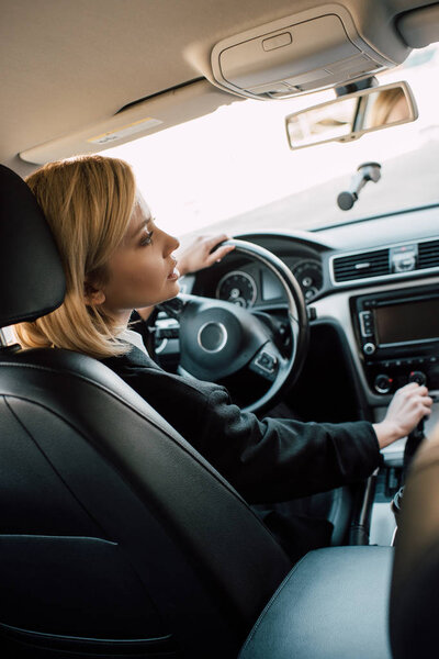 blonde young woman holding gear shift handle while sitting in car 