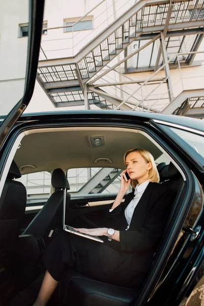 Arabada Dizüstü Bilgisayar Ile Otururken Akıllı Telefon Konuşurken Endişeli Sarışın — Stok fotoğraf