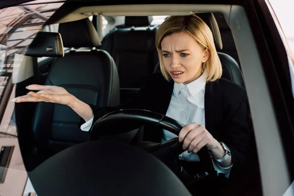心烦意乱的金发女孩拿着方向盘 而手势和驾驶汽车 — 图库照片