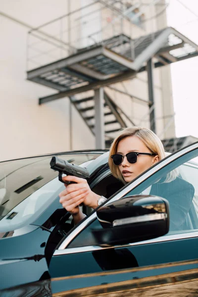 Серьезная Блондинка Солнечных Очках Пистолетом Возле Черной Машины — стоковое фото