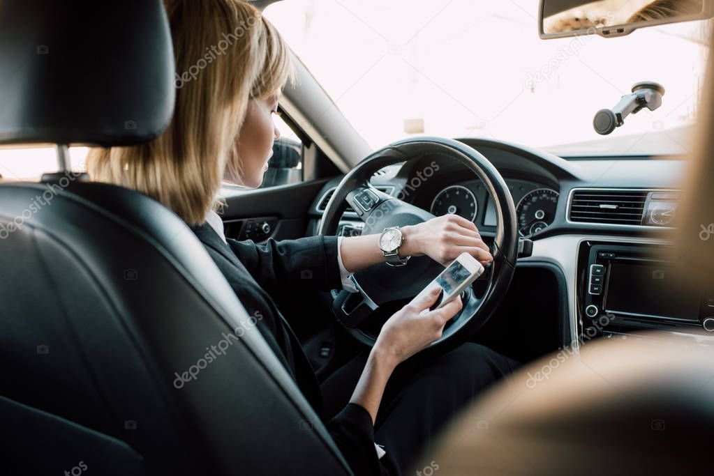 blonde young woman sitting in car and holding smartphone 