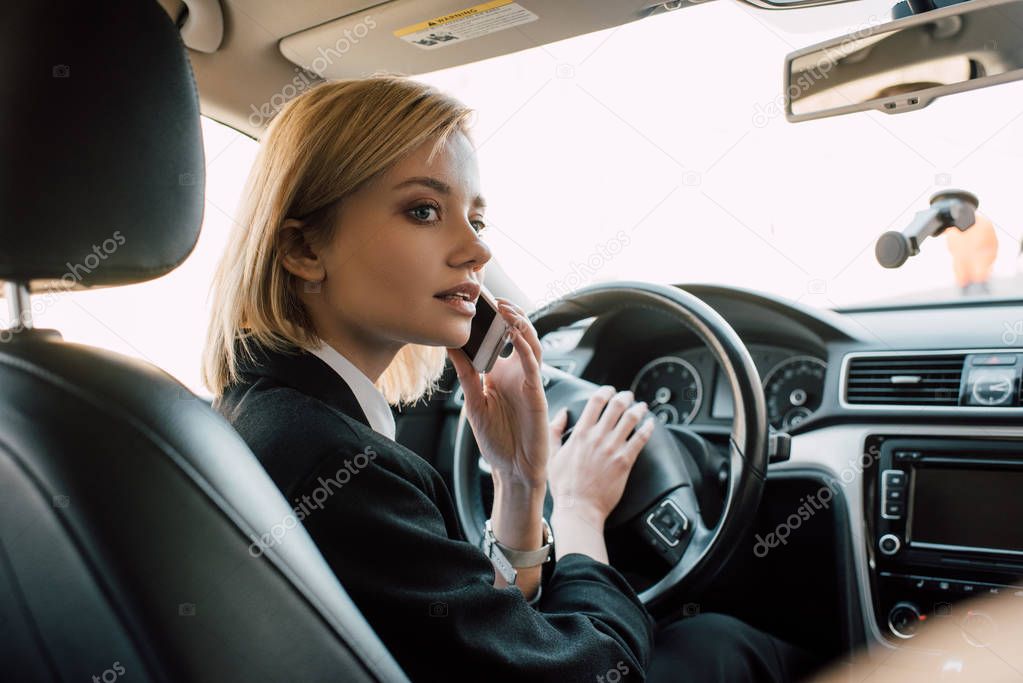 blonde young woman sitting in car and talking on smartphone 