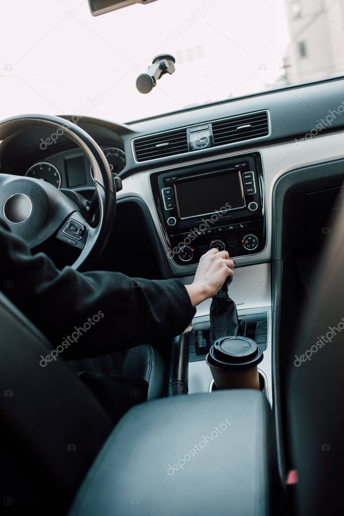cropped view of woman holding gear shift handle while sitting in car 