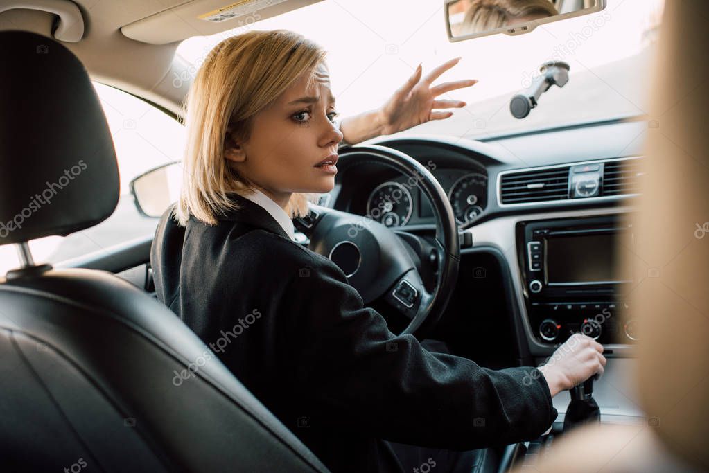 worried blonde woman gesturing while sitting in car 
