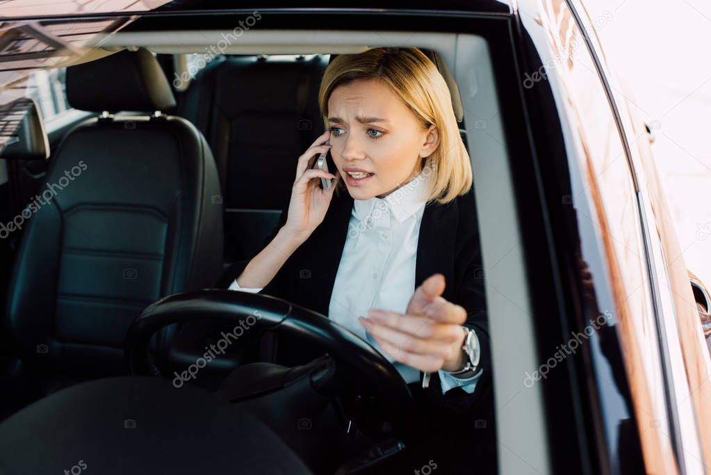upset blonde woman talking on smartphone while gesturing in car 