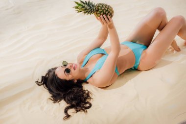 mavi Bikini ve güneş gözlüğü ananas ile kumlu plajda yalan güzel gülümseyen kız 