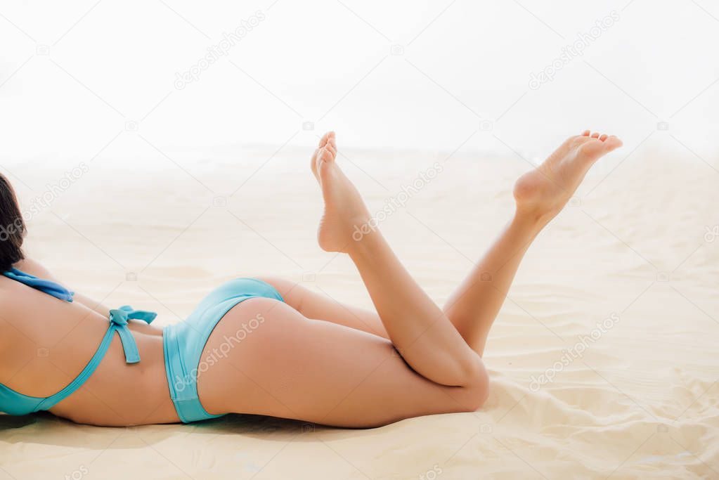 cropped view of sexy girl in blue Bikini relaxing on sandy beach