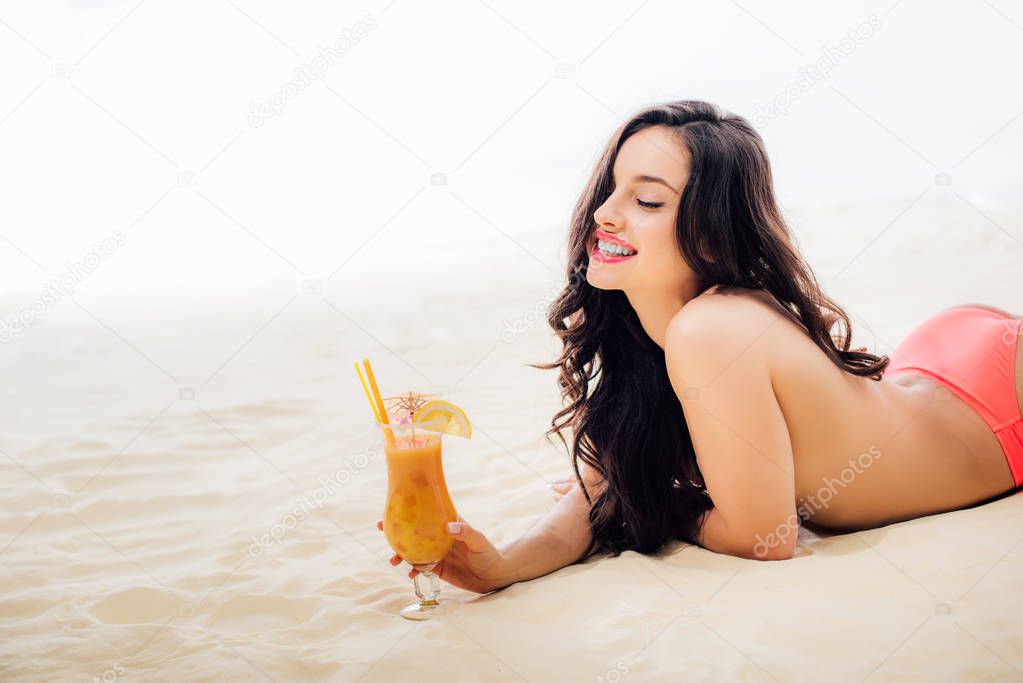 beautiful smiling topless girl with cocktail lying on beach with copy space