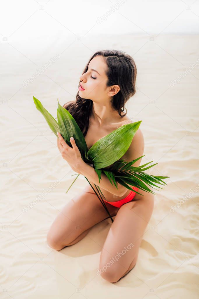 beautiful sexy girl covering breasts with leaves and posing on beach