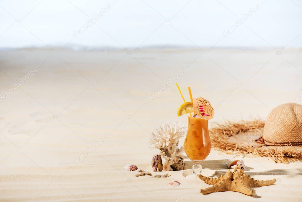 cocktail, starfish, Straw Hat, coral and sea stones on sandy beach with copy space