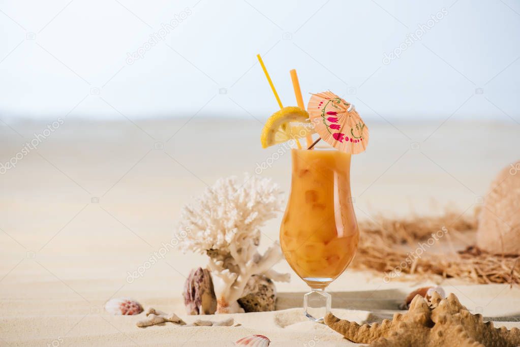 cocktail, starfish, coral and sea stones on sandy beach