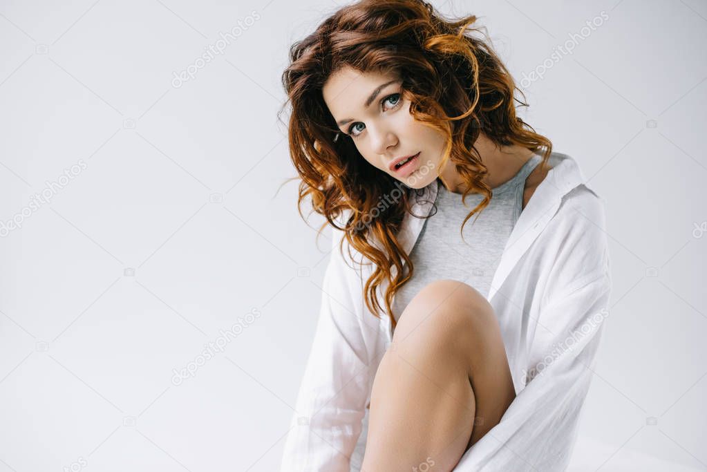 pretty woman with curly red hair sitting and looking at camera on white 