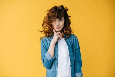 beautiful curly young woman touching cheek while standing on orange   clipart