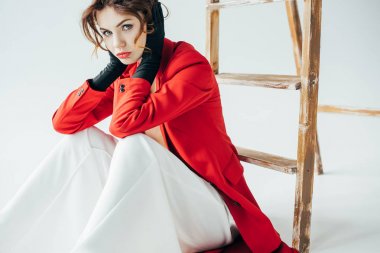 kırmızı saçlı üzgün ve trendy genç kadın kameraya bakarak ve beyaz merdivenin yanında oturan 