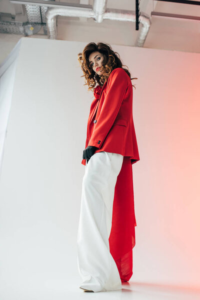 low angle view of stylish and beautiful curly girl looking at camera on grey with gradient 