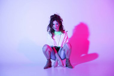 kızıl saçlı şık kız oturan ve aydınlatma ile mor kamera bakıyor 