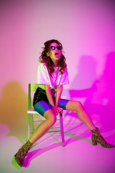 선글라스를 착용한 매력적인 여성이 의자에 그라데이션을 보라색에 보이고 있습니다 — 스톡 사진