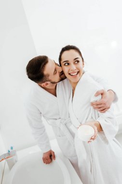 neşeli adam sarılma ve yüz kremi ile konteyner tutan mutlu kız arkadaşı yanak öpüşme 