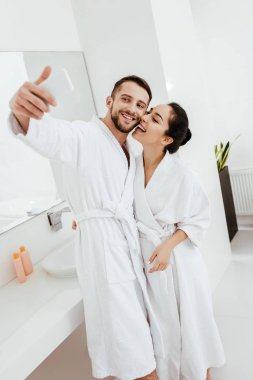 neşeli çift bornoz ayakta selfie ve gülümseyerek 