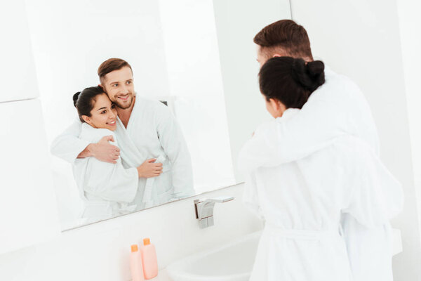 selective focus of happy man hugging attractive brunette woman while looking at mirror 