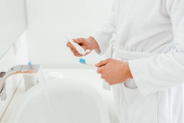 banyoda lavabo yakınında diş fırçası ve diş macunu tutan adam kırpılmış görünümü 