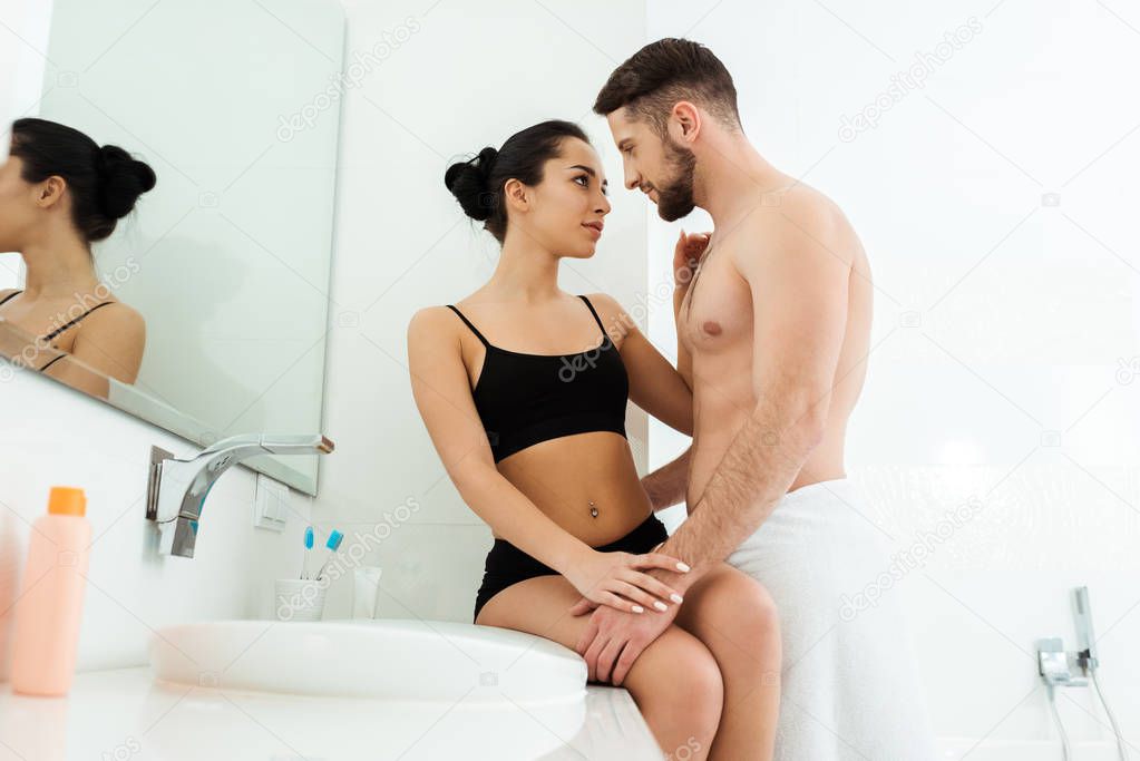 low angle view of handsome shirtless man looking and touching attractive girlfriend in black underwear 